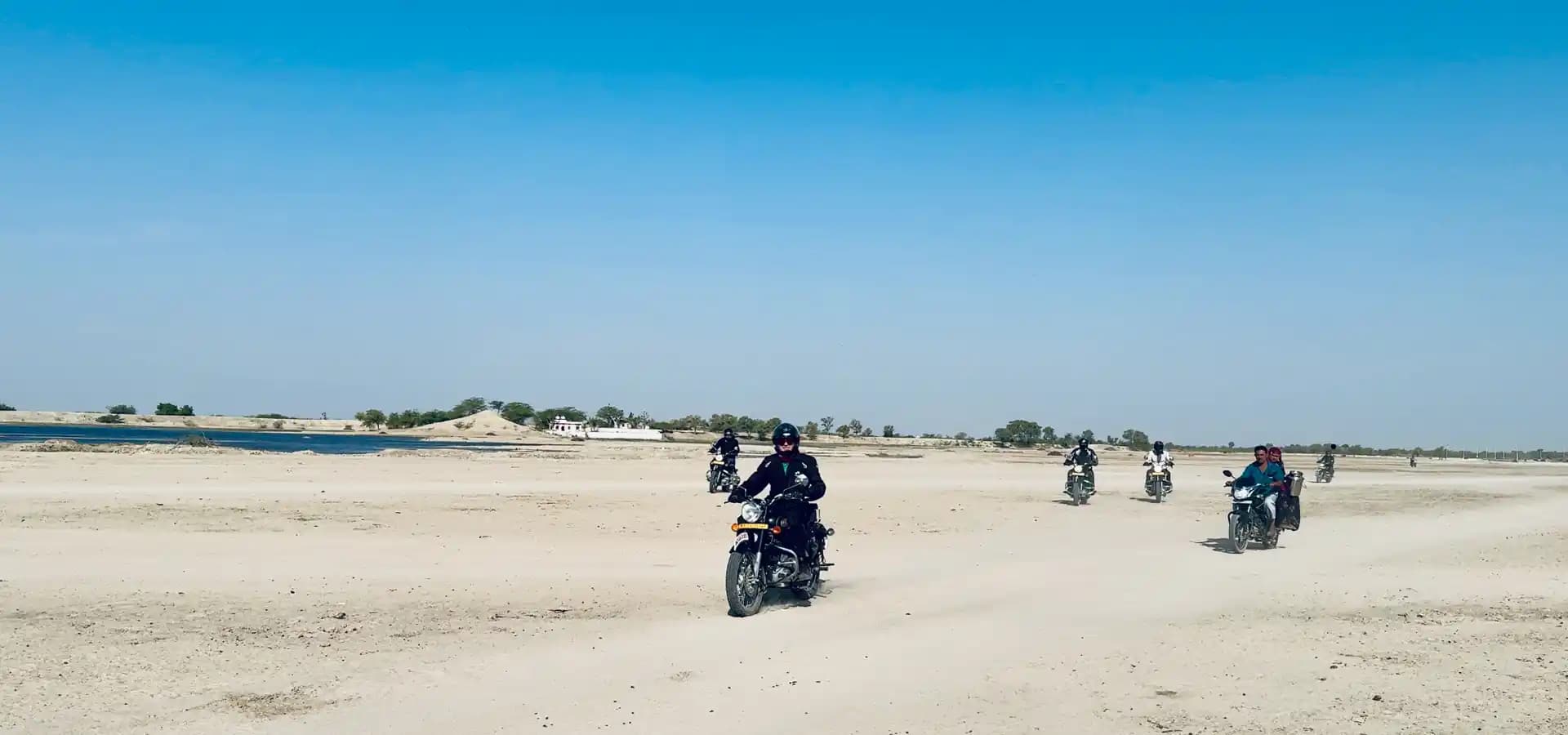 Royal Enfield Motorcycle Tour Through Rajasthan Riders on Royal Enfield motorcycles crossing a desert landscape in Rajasthan, India